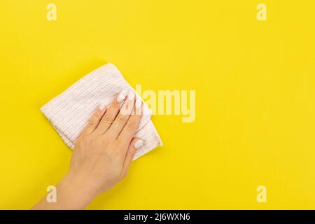 La main d'une femme au foyer tient un chiffon pour épousseter ou laver. Espace vide pour le texte ou le logo sur fond jaune. Début du printemps ou nettoyage régulier. Nettoyage Banque D'Images