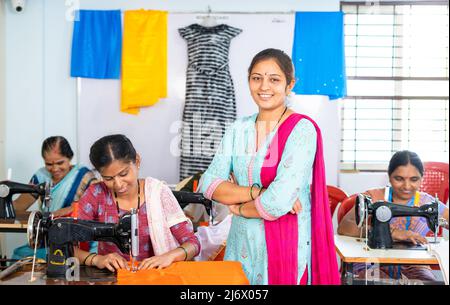 Souriantes femmes debout avec les bras croisés devant les travailleurs en regardant la caméra des vêtements - concept de travailleurs confiants, réussis et petits Banque D'Images