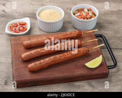 Brochettes de saucisse de porc sur une planche de bois avec farofa, citron et vinaigrette. Banque D'Images