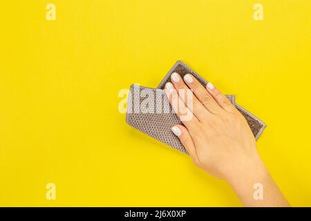 La main d'une femme au foyer tient un chiffon pour épousseter ou laver. Espace vide pour le texte ou le logo sur fond jaune. Début du printemps ou nettoyage régulier. Nettoyage Banque D'Images