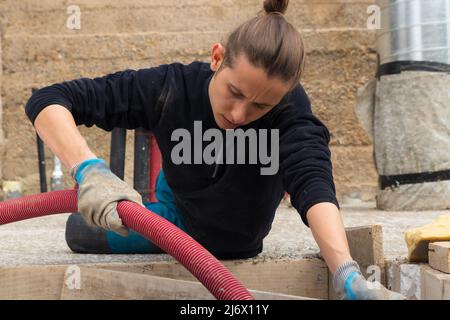 Perperctif horizontal de jeunes électriciens dans les pratiques de pose sur un sol en béton tenant un tube rouge pour passer des câbles Banque D'Images