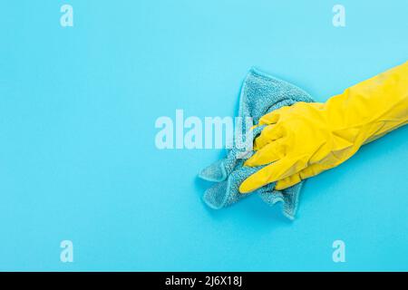 main de travail dans un gant de protection en caoutchouc jaune avec un chiffon en microfibre bleu essuyant un mur bleu de la poussière. Une femme de ménage prend soin de la maison. Banque D'Images