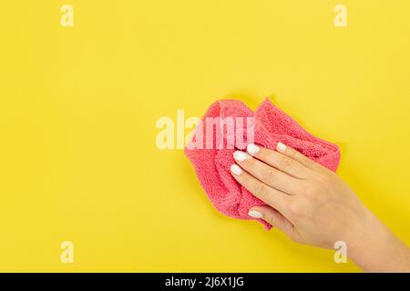 La main d'une femme au foyer tient un chiffon pour épousseter ou laver. Espace vide pour le texte ou le logo sur fond jaune. Début du printemps ou nettoyage régulier. Nettoyage Banque D'Images