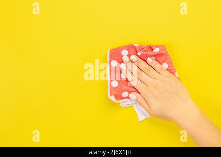 La main d'une femme au foyer tient un chiffon pour épousseter ou laver. Espace vide pour le texte ou le logo sur fond jaune. Début du printemps ou nettoyage régulier. Nettoyage Banque D'Images