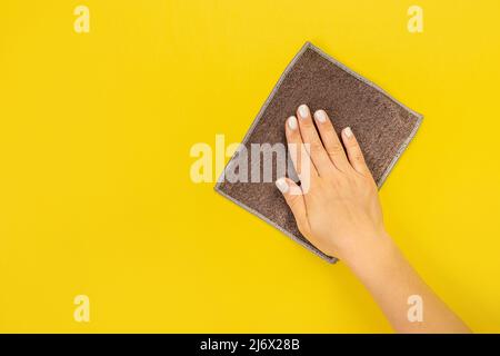 La main d'une femme au foyer tient un chiffon pour épousseter ou laver. Espace vide pour le texte ou le logo sur fond jaune. Début du printemps ou nettoyage régulier. Nettoyage Banque D'Images