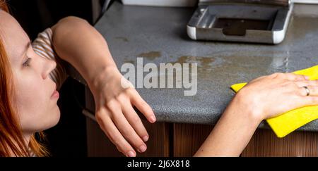 La machine à café est en panne et doit être réparée. La femme essuye les conséquences avec un chiffon. Fuite, déversement de café sur la table de cuisine Banque D'Images