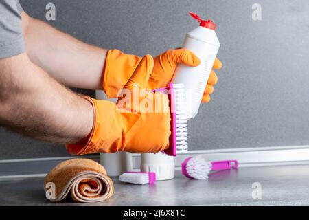 Homme et concept de nettoyage. La main d'un homme tient un geste d'approbation avec une main dans un gant en caoutchouc contre le fond des produits de nettoyage sur le kit Banque D'Images