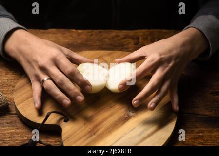 moitiés d'un oignon brut dans les mains d'une femme sur fond de bois. Banque D'Images