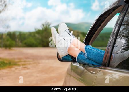 Les jambes des sneakers blanches dépassent de la fenêtre de la voiture, en gros plan. Le concept de voyage en voiture. Banque D'Images
