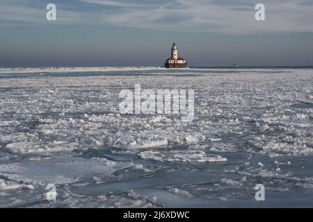 Lumière froide d'hiver sur le lac Michigan avec des formations de glace à crêpes et un phare au loin Banque D'Images