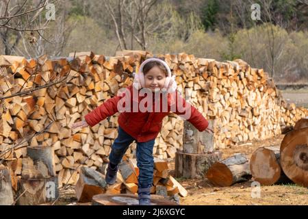 Petite fille jouant sur des bûches en bois, debout sur le fond du mur de bois de chauffage. Vie de pays Banque D'Images