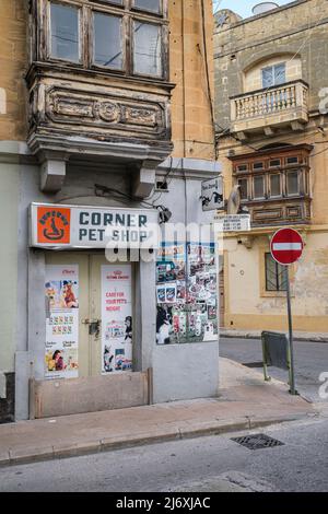 Un coin de rue à Tarxien avec une animalerie et des balcons maltais traditionnels sur des bâtiments délabrés, Tarxien, Malte Banque D'Images