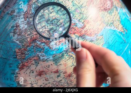 Main avec loupe zoom Ukraine sur la carte du monde avec la langue russe. Banque D'Images