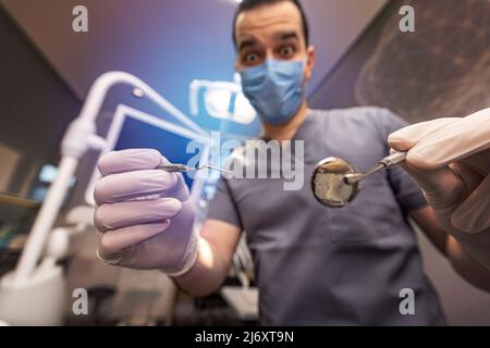 Dentiste de sexe masculin dans un masque facial avec des outils debout dans une clinique dentaire Banque D'Images