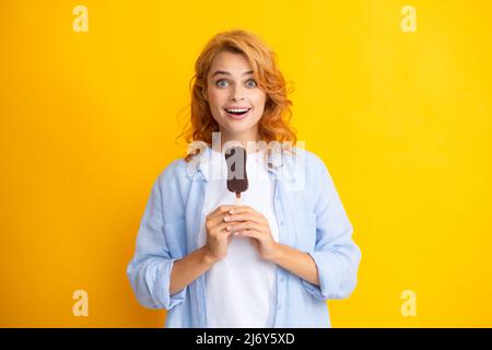 La jeune femme mange des crèmes glacées au chocolat sur fond jaune. Drôle femme de tête rouge avec de la crème glacée. Stupéfait surprise visage de femme. Banque D'Images