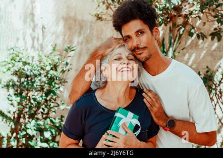 Bonne famille interraciale. Son fils donne un cadeau à sa mère dans le jardin de la maison. Banque D'Images