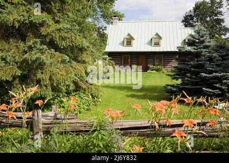 Ancienne maison en rondins de style Canadiana 1800s avec cour avant paysagée protégée par une clôture en bois rustique. Banque D'Images