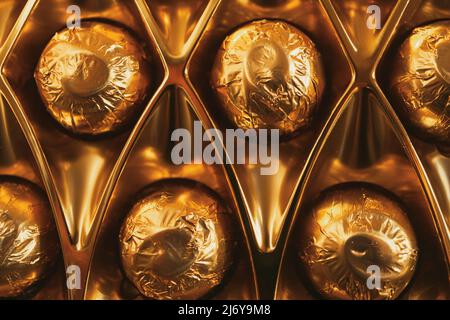 Gros plan des bonbons au chocolat emballés dans du papier d'aluminium doré dans leur boîte Banque D'Images