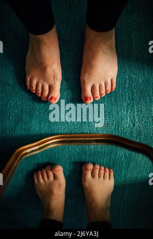 pieds avec crapaud peint en rouge sur la moquette sarcelle et miroir à bordure dorée Banque D'Images