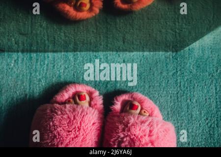 pieds avec crapaud rouge peint dans des chaussons flous à fourrure rose contre le tapis de sarcelle Banque D'Images