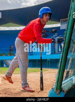 Un joueur de baseball cubain en route pour la batte parle à un coéquipier du dugout dans un stade de la Havane, Cuba. Banque D'Images