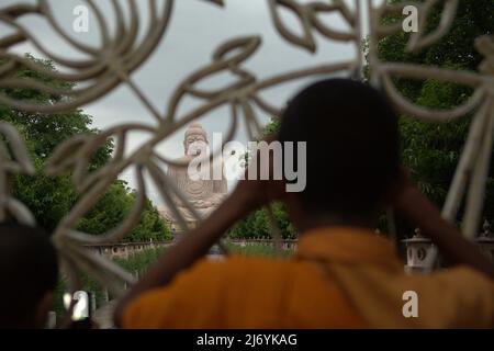 Un moine faisant attention à une statue de 64 pieds de haut du Grand Bouddha derrière la clôture à Bodh Gaya, Bihar, Inde. Il a été construit dans une pose de méditation à partir d'un mélange de grès et de granit rouge par l'artiste V. Ganapati Sthapati de 1982 à 1989. Banque D'Images