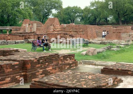 Visiteurs assis sur un banc au milieu de ruines de structures en briques au complexe Dhamek stupa à Sarnath, à la périphérie de Varanasi, Uttar Pradesh, Inde. Banque D'Images