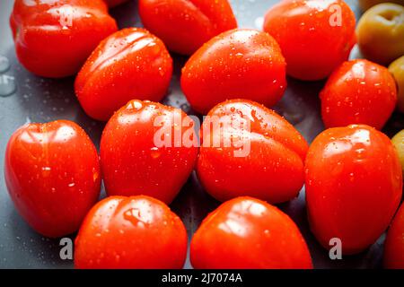 Groupe de tomates cerises mûres humides avec des gouttes sur une assiette noire, vue du dessus Banque D'Images