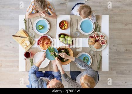 Directement au-dessus de la vue de la famille caucasienne assis à table et ayant un délicieux dîner: Salade de légumes frais, fruits, fromage et tarte maison Banque D'Images