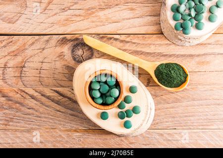 comprimés ronds verts de spiruline sur une plaque en bois naturel et dans une cuillère sous forme de piston. vue de dessus. concept de renforcement du corps Banque D'Images