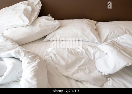 Intérieur de la chambre d'hôtel le matin avec un lit désordonné. Linge de lit blanc froissé, oreillers et couverture sur le lit Banque D'Images