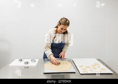 Chef pâtissier dans un tablier coupant la pâte tout en faisant des biscuits dans la cuisine de boulangerie. Banque D'Images