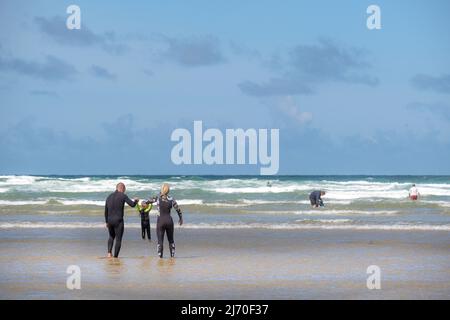 Une mère et un père tenant la main avec leur enfant en bas âge pagayant dans la mer à Mawgan Porth, dans les Cornouailles; une fête de cornouailles pour les familles. Banque D'Images