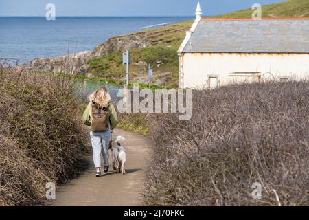 Vue arrière d'une jeune femme avec un sac à dos qui marche son chien le long du sentier côtier à Newquay, en Cornouailles, au Royaume-Uni. Banque D'Images