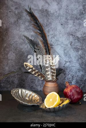 Composition abstraite de plumes d'oiseau dans un pichet en céramique, grenade et citron. Banque D'Images