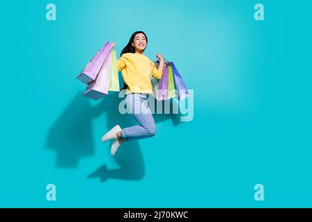 Photo pleine longueur de douce jolie dame vêtue jaune chandail sautant les shoppers montant vide espace isolé couleur turquoise arrière-plan Banque D'Images