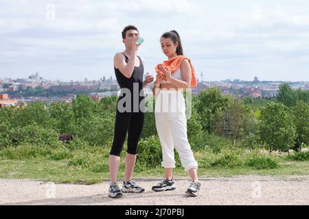 Jeune couple sportif qui boit de l'eau et une serviette sur la transpiration dans un parc. Banque D'Images