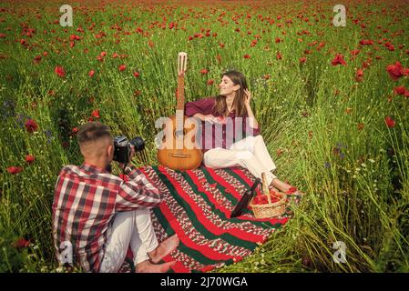 couple amoureux de faire des photos sur caméra avec guitare acoustique dans le champ de fleurs de pavot d'été, temps libre. Banque D'Images