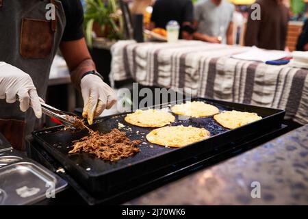 Un homme grille des tacos de bœuf et de fromage sur un marché, à main levée Banque D'Images