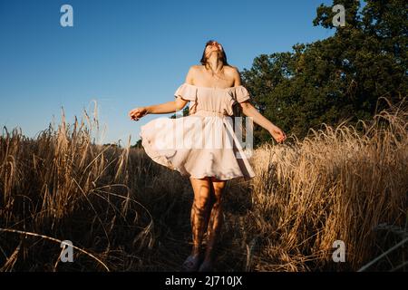 Connectez-vous à la nature, ralentissez, soyez présent, entrez dans vos sens. Paisible seule jeune femme en robe marchant sur le champ de blé au coucher du soleil le jour d'été Banque D'Images