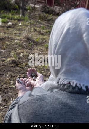 Une femme âgée dans un mouchoir avec des pièces de monnaie roubles dans ses mains est assise avec son dos à la caméra. Concentrez-vous sur les mains. Banque D'Images