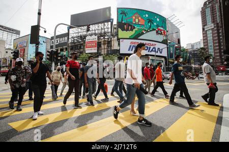 Des piétons portant un masque facial sont vus traverser la rue près d'un centre commercial pendant les vacances d'Eid al-Fitr à Kuala Lumpur. Banque D'Images