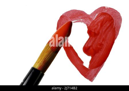 Pointe de la brosse de l'artiste trempée en acrylique rouge sur coeur peint partiellement terminé sur fond blanc Banque D'Images