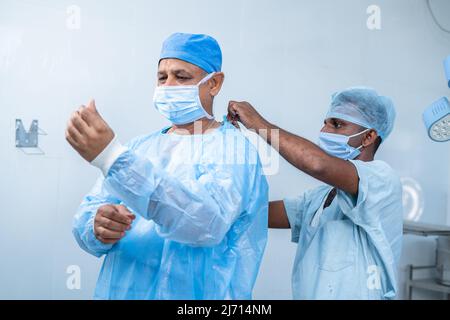 Infirmière aidant le chirurgien à porter une robe au théâtre d'opération pour la chirurgie - concept de profession professionnelle, expertise et personnel de soutien. Banque D'Images