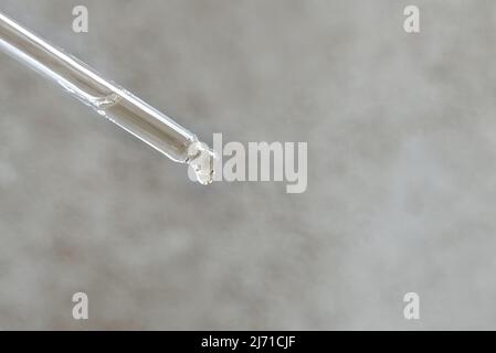 Pipette en verre transparent avec huile essentielle ou sérum sur fond de béton gris clair. Une goutte d'huile cosmétique tombe. Copier l'espace. Banque D'Images