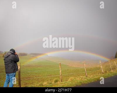 Homme prenant des photos d'un double arc-en-ciel sur le plateau aubrac lozère France sous la pluie . Banque D'Images