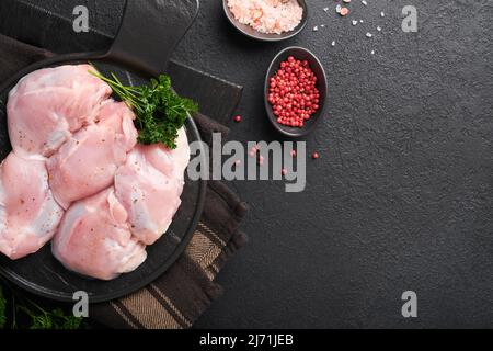 Filet de cuisse de poulet cru sans peau avec herbes et épices sur fond noir. Viande de volaille agricole. Vue de dessus avec espace de copie. Maquette. Banque D'Images