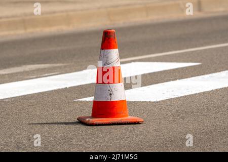 Cône de circulation avec bandes orange et blanches sur la rue sur asphalte gris pendant les travaux de construction routière. Je viens de peindre des lignes de rue blanches sur des pades Banque D'Images