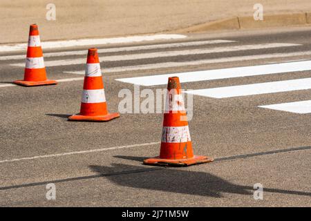 Cônes de signalisation avec bandes orange et blanches sur la rue sur asphalte gris pendant les travaux de construction de routes. Je viens de peindre les lignes blanches sur le papede Banque D'Images