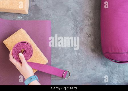 Tapis de yoga ouvert, bloc de liège, main de femme avec sangle de yoga et traversin. Notions de base sur les accessoires de yoga. Copier l'espace. Banque D'Images